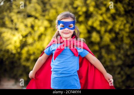 Superhero kid girl against green background outdoor. Childhood, success and and power concept Stock Photo