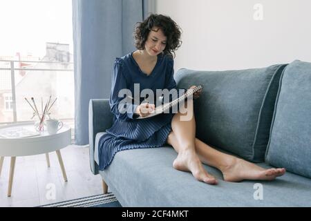 Elegant Woman sitting on a sofa drawing on a notebook at home Stock Photo