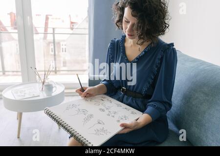 Elegant Woman sitting on a sofa drawing on a notebook at home Stock Photo