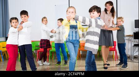 Group of cheerful school kids learning to dance in pairs with their teacher in classroom on recess Stock Photo