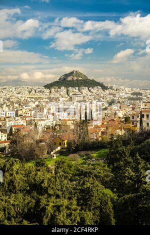 Apartment buildings located near green mountain peak on cloudy day in Athens, Greece Stock Photo
