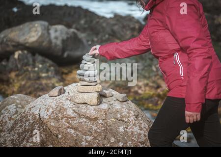 Side view of crop anonymous Woman in jacket making stone building from small rocks during trip around Northern Ireland Stock Photo