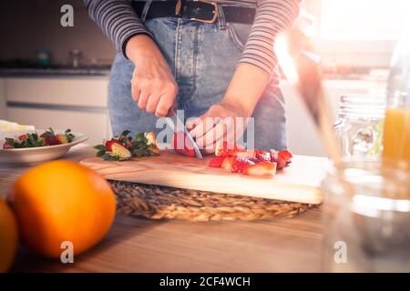 unrecognizable female in casual outfit chopping fresh strawberries in a kitchen Stock Photo