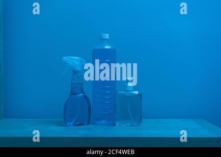 Plastic transparent bottles of different sizes and shapes with colorless liquid inside and white lids locating on shelf against blue wall Stock Photo