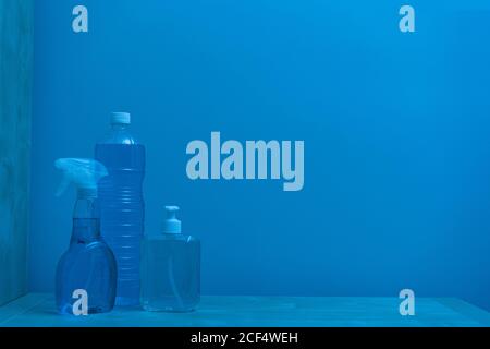 Plastic transparent bottles of different sizes and shapes with colorless liquid inside and white lids locating on shelf against blue wall Stock Photo