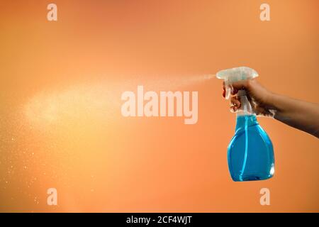 anonymous person with spray in plastic bottle for disinfection of surfaces pulverizing liquid on orange background in studio Stock Photo