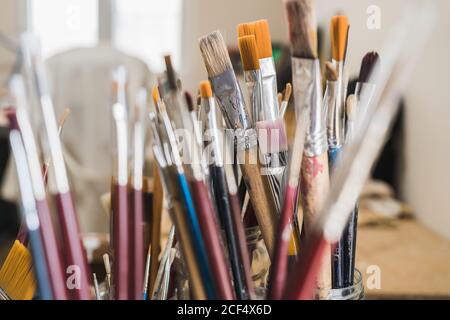 Set of various multi colored artists paintbrushes locating in glass on wooden table of modern art workshop on sunny day