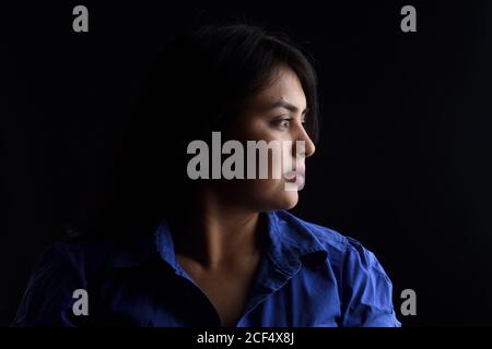 side view of dark portrait of a latin woman on black background, serious Stock Photo