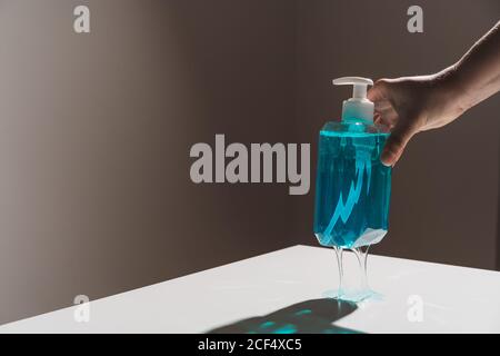Plastic transparent bottle with blue liquid soap located on white surface and thin soap stream coming out of white dispenser Stock Photo