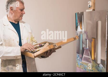 Senior artist standing in home workshop and choosing paints Stock Photo