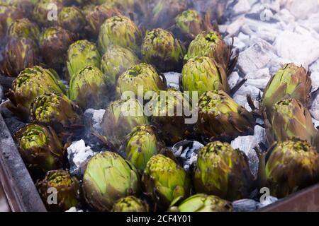 Closeup of artichokes being grilled on burning charcoal in brazier Stock Photo