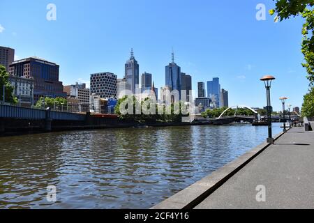 Looking along the Yarra River in downtown Melbourne from the Southbank Promenade. It is a clear sunny day and no pedestrians walk along the river bank Stock Photo
