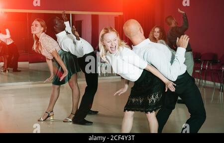 Young smiling people practicing vigorous jive movements in dance class Stock Photo