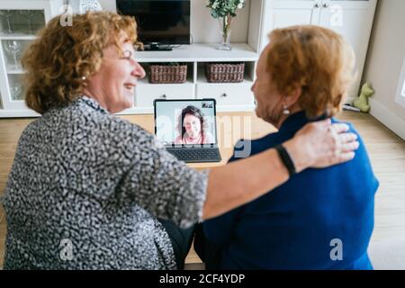 Back view of cheerful senior women chatting with friend during online video meeting via laptop while staying at home during coronavirus lockdown Stock Photo