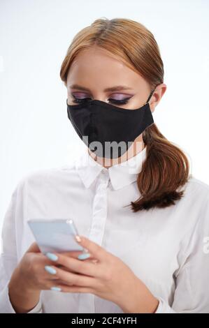 Girl using smartphone wearing black face mask isolated on white studio background Stock Photo