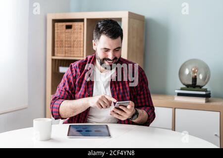 A young man is typing on the mobile phone. The man is working from home. The entrepreneur is using his phone and smiling Stock Photo