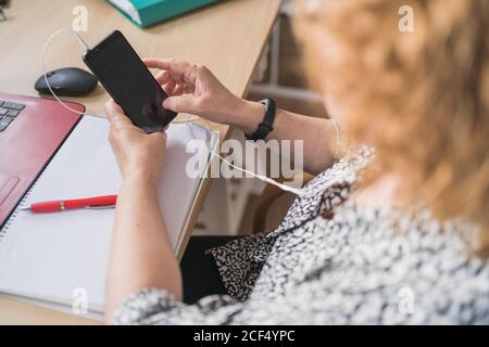 From above view of anonymous female freelancer in casual clothes typing on keyboard while working with laptops at wooden table at home Stock Photo