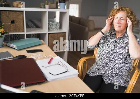 Side view of focused adult Woman in casual clothes enjoying music in earphones with closed eyes while resting during work on laptop and notebook Stock Photo