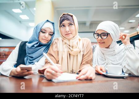 Three muslim Women in hijab sitting at table, and writing Stock Photo