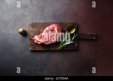 Top view of raw black angus prime rib eye beef steak on wooden cutting board.