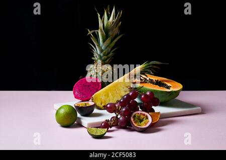 Still life with tropical fruits: sliced papaya, pineapple, pitaya and grapes on marble cutting board Stock Photo