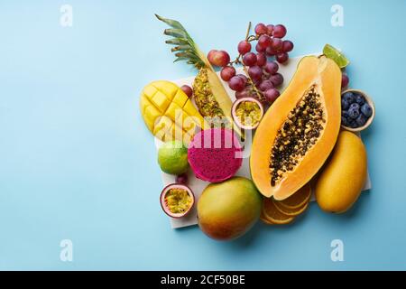 Top view of flat lay with tropical fruits on a tray: papaya, mango, dragon fruit and pineapple on blue background. Summer treat Stock Photo