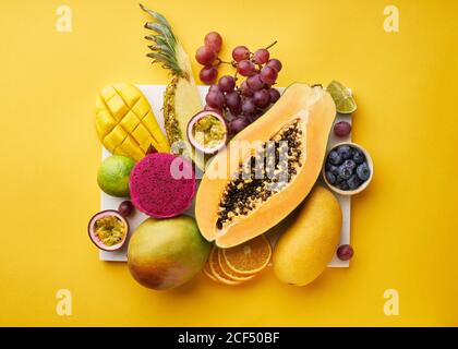 Top view of flat lay with tropical fruits on a tray: papaya, mango, dragon fruit and pineapple on yellow background. Summer treat Stock Photo