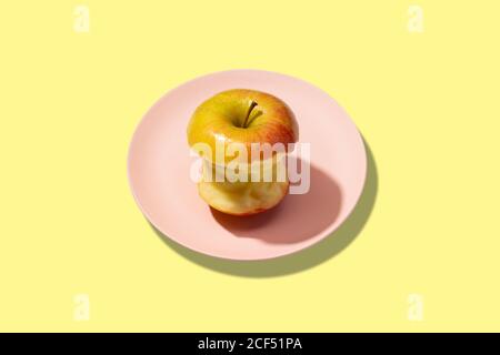 Fresh bitten apple in plate on yellow background. Vibrant colorful pattern Stock Photo