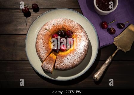 Round cherry cake in plate on wooden table. Dark food Stock Photo
