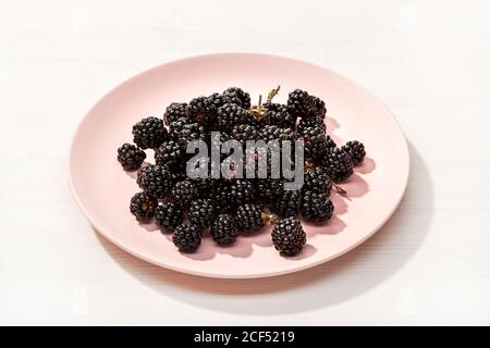 Fresh wild blackberries in plate on white wooden background. Edible wild fruit Stock Photo