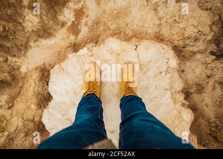 From above top view of anonymous person legs in brown boots and blue jeans standing on dirty sandy road with mountain and sky on blurred background in Bardenas Reales, Navarre, Spain Stock Photo