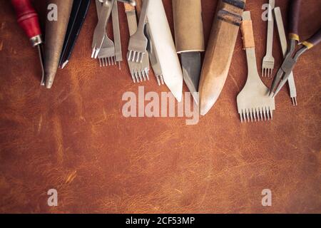 Leather craft tools on a wooden background. Leather craftmans work desk . Piece of hide and working handmade tools on a work table.copyspace Stock Photo
