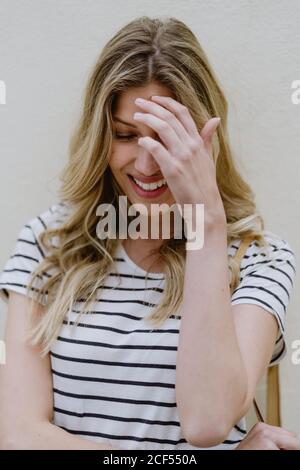 Close-up portrait of charming young long haired blonde female wearing striped shirt and jeans looking down with shyly smile Stock Photo