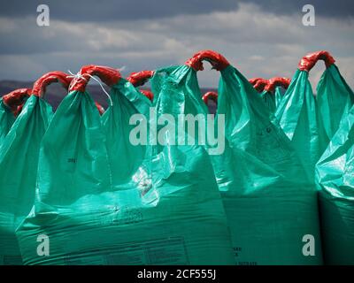 Orange plastic handles on large blue green bags of agricultural fertiliser contrast with dark threatening skies on farmland in Cumbria, England, UK Stock Photo