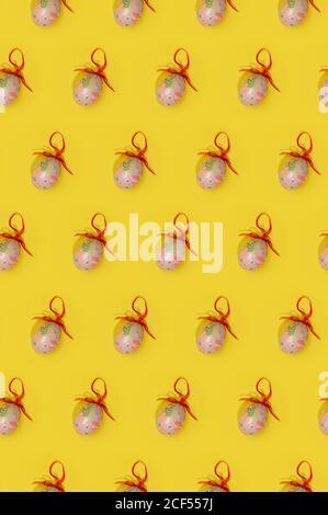 Seamless Easter pattern with colorful eggs decorated with red ribbons arranged in rows on yellow background Stock Photo