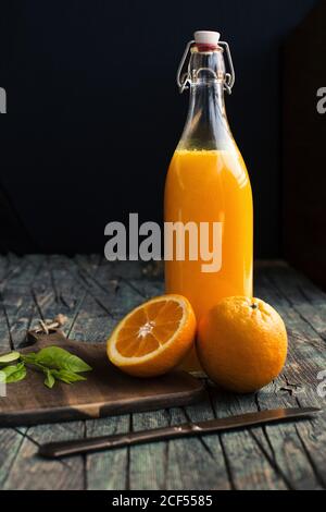 Bottle of fresh citric orange juice placed near halves of fresh oranges on a wooden dark rustic table at dark background Stock Photo