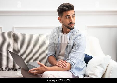 Bearded ethnic man using laptop while working on remote project at home sitting on the sofa Stock Photo