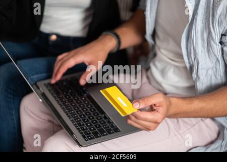Cropped unrecognizable man hands sitting on sofa and making online purchases with credit card on a laptop Stock Photo