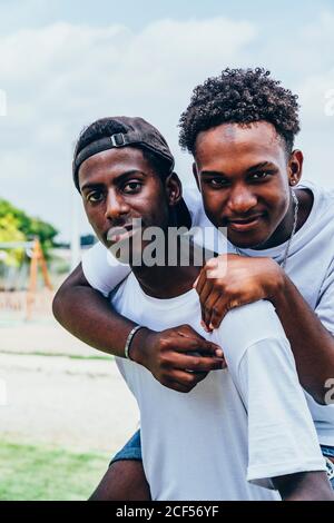 Cheerful hugging African American young men looking at camera and gesturing Stock Photo