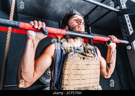 Strong man doing pull-up exercise with weight on horizontal bar Stock Photo