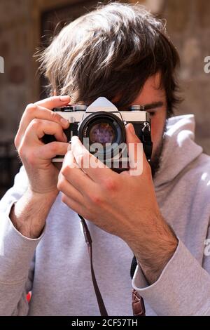 Positive man in casual outfit with camera adjusting optics for photoshoot while standing outside Stock Photo