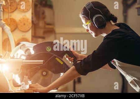 Attractive female carpenter using some power tools for her work in a woodshop Stock Photo