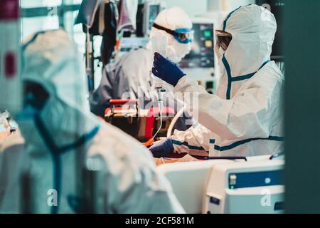 Side view of doctor wearing protective uniform and latex gloves checking infusion system while working in modern clinic Stock Photo