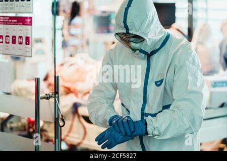 Professional doctor in protective white uniform and mask putting on latex gloves before operation in modern surgery room in hospital Stock Photo