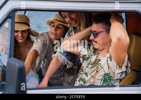 Lively cheerful ladies in hat pointing on road in map while man trying to choose right way in car in bright day Stock Photo