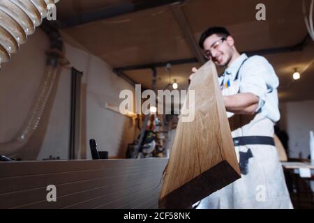 Expert carpenter in his workshop, looking down the length of a wooden plank, checking it for quality and straightness Stock Photo
