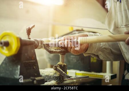 young man with dark hair and goggles holds a stalker in his hands and processes a wooden product on a lathe in the workshop Stock Photo