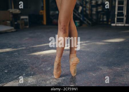 Crop unrecognizable female ballet dancer in pointes with bruise on leg standing on tiptoe while performing classic exercise during training in studio Stock Photo