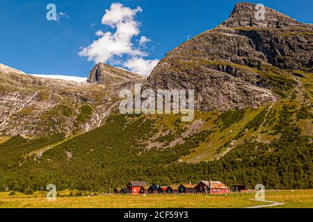 A remote settlement lies here near Lake Lovatnet, close to Stryn, Norway. Meadows and pastures stretch up the slope, with rugged mountain peaks rising in the background. Stock Photo