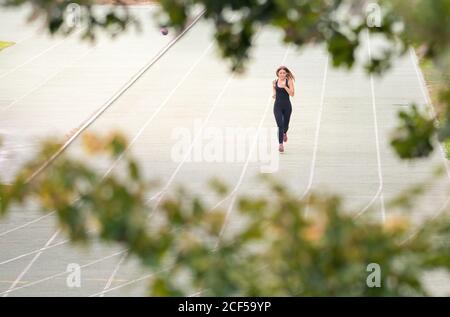 view between trees of a young fit Woman running in a track outdoors in a sunny day Stock Photo